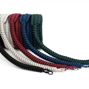 May include: A set of six camera straps in different colors, including black, white, red, blue, dark blue, and green. The straps are made of braided paracord and have metal clasps.