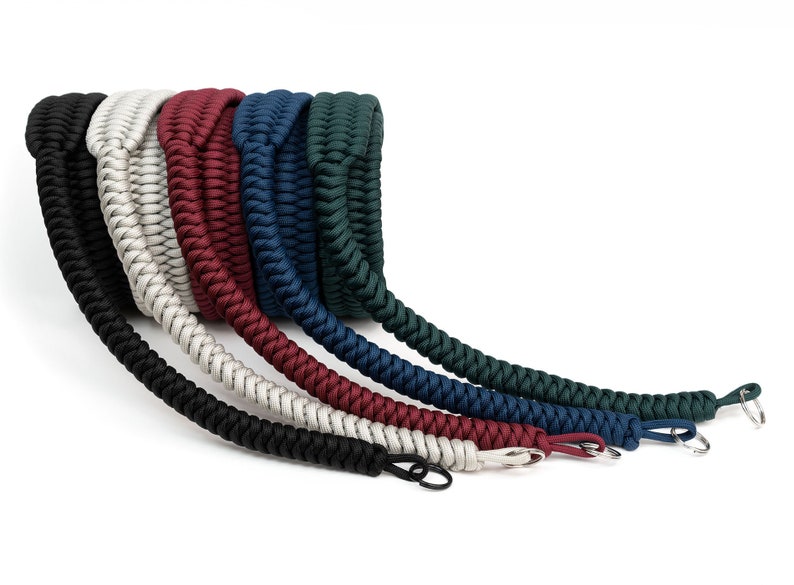 May include: A set of six camera straps in different colors, including black, white, red, blue, dark blue, and green. The straps are made of braided paracord and have metal clasps.
