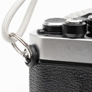 May include: A silver camera with a black leather covering and a white strap attached to a metal ring.