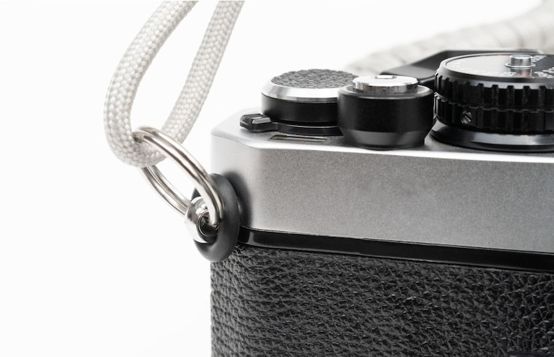 May include: A silver camera with a black leather covering and a white strap attached to a metal ring.