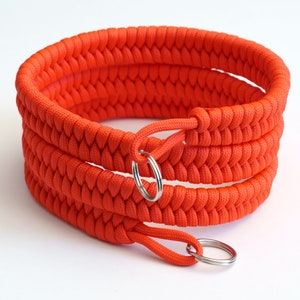 May include: A bright orange paracord bracelet with two silver key rings. The bracelet is made with a woven pattern.