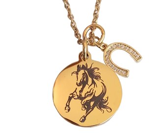 May include: Gold-coloured necklace with a round pendant depicting a horse silhouette and a horseshoe charm. The horseshoe is adorned with small, clear crystals. The necklace has a fine chain.