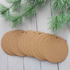 May include: Ten brown round craft paper gift tags with a hole punched in the top. The tags are arranged in a row on a white wooden surface.