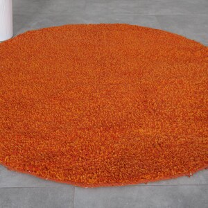 May include: A round, orange, fluffy rug with a soft, plush texture.