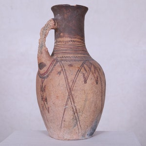 Peut inclure: Une cruche en céramique brune avec une anse cassée, décorée de motifs géométriques en peinture rouge et blanche.