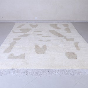 May include: A white shag rug with a beige abstract pattern. The rug has a fringe border.