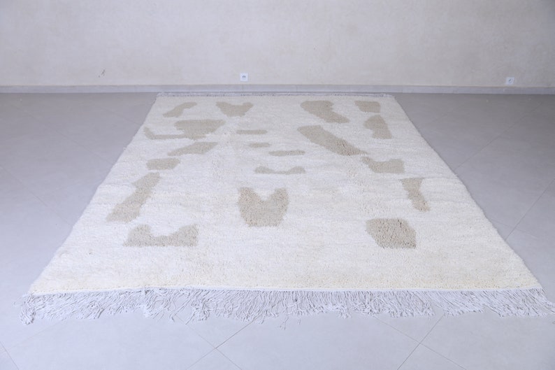 May include: A white shag rug with a beige abstract pattern. The rug has a fringe border.