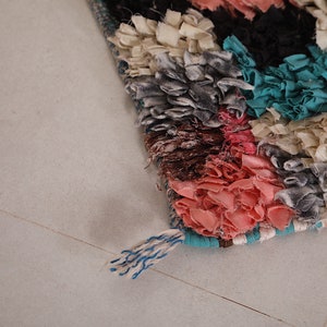 Puede incluir: Una alfombra colorida tejida a mano con un detalle de flecos. La alfombra est&aacute; hecha de varias telas en tonos de rosa, azul, blanco y gris.