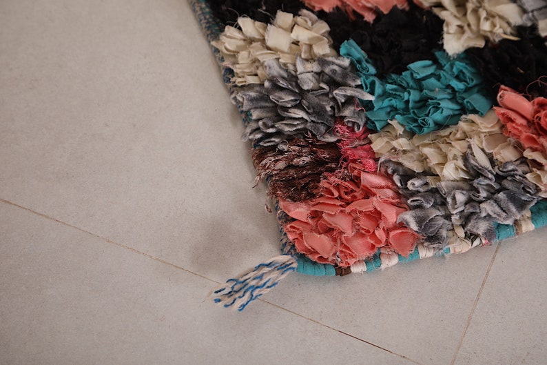 Puede incluir: Una alfombra colorida tejida a mano con un detalle de flecos. La alfombra est&aacute; hecha de varias telas en tonos de rosa, azul, blanco y gris.