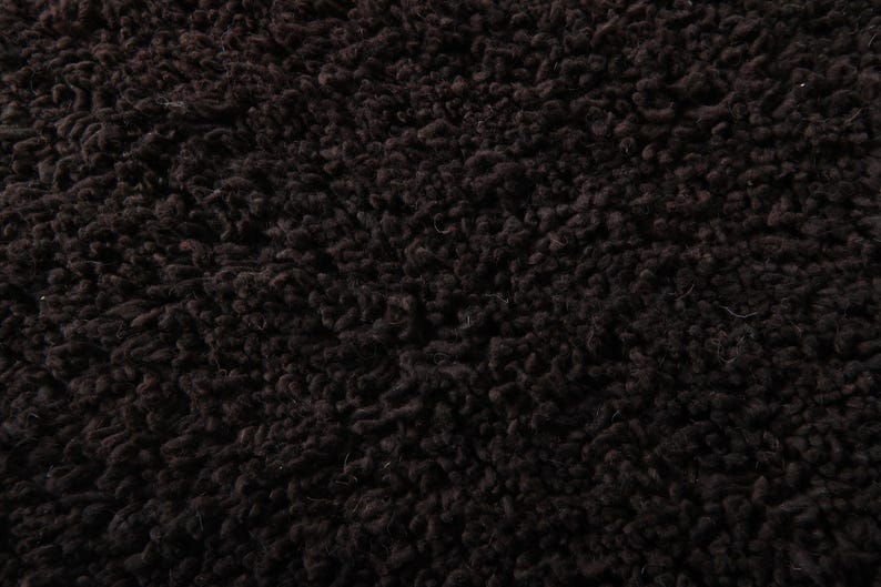 May include: Close-up of a dark brown, textured fabric with a dense, looped pile. The material has a soft, plush appearance, with a slightly uneven surface. The overall effect is a rich, warm texture.