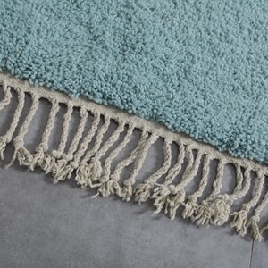 May include: A light blue round rug with a white fringe border. The rug is made of a soft, fluffy material.