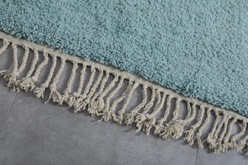 May include: A light blue round rug with a white fringe border. The rug is made of a soft, fluffy material.