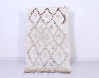 May include: A white and brown Moroccan rug with a diamond pattern. The rug has a fringed border.