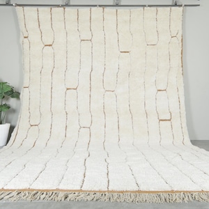 May include: Cream-colored rug with a vertical rectangular pattern and a fringed edge. The rug has a textured, plush appearance and is displayed against a neutral backdrop. The design features brown accents within the rectangular shapes.