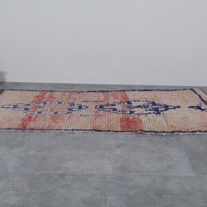 May include: A vintage, hand-woven rug with a geometric pattern in shades of blue, red, and white. The rug has a distressed, worn look and is made of natural fibers.