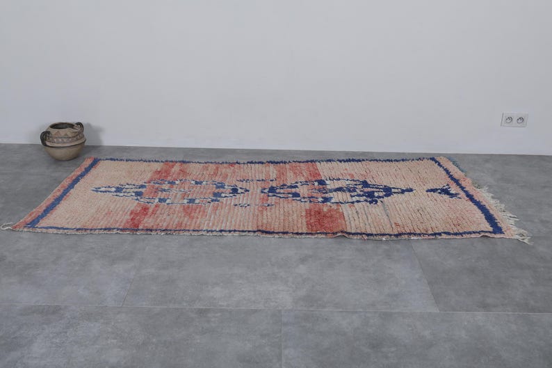 May include: A vintage, hand-woven rug with a geometric pattern in shades of blue, red, and white. The rug has a distressed, worn look and is made of natural fibers.