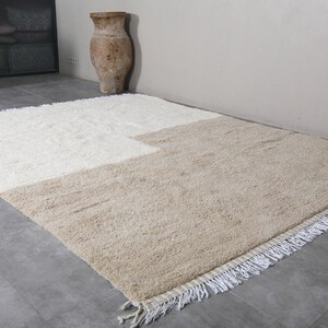 Puede incluir: Una alfombra de pelo blanco y beige con borde de flecos. La alfombra est&aacute; dividida en dos secciones, una blanca y una beige.