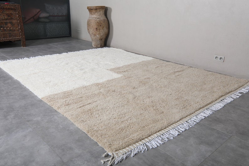 Puede incluir: Una alfombra de pelo blanco y beige con borde de flecos. La alfombra est&aacute; dividida en dos secciones, una blanca y una beige.