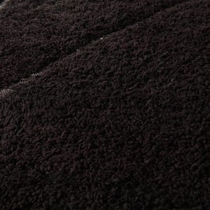 May include: Close-up of a dark brown, textured fabric. The material has a dense, looped pile, creating a soft, plush appearance. A lighter, textured area is visible, possibly a seam or a different fabric section.