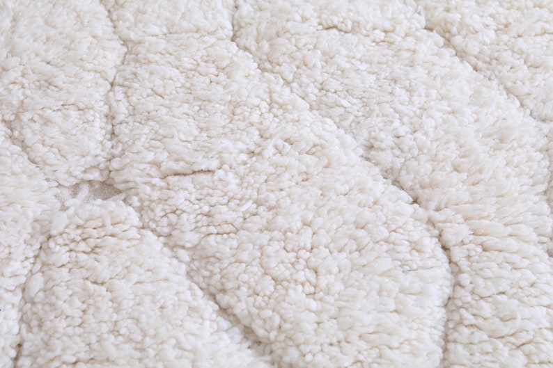 May include: Close-up of a white, fluffy, textured fabric with a wavy pattern. The fabric is soft and plush, resembling a sheepskin rug.