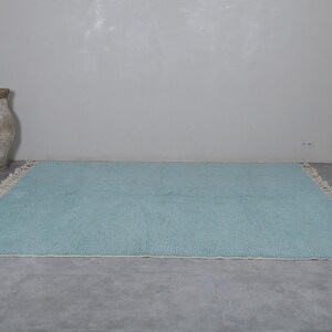 May include: A light blue rug with a white fringe border. The rug is laid out on a gray concrete floor.