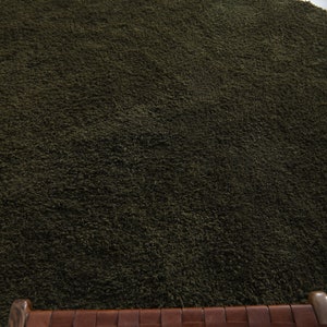 May include: A dark green shag rug with a woven leather seat cushion in front of it.