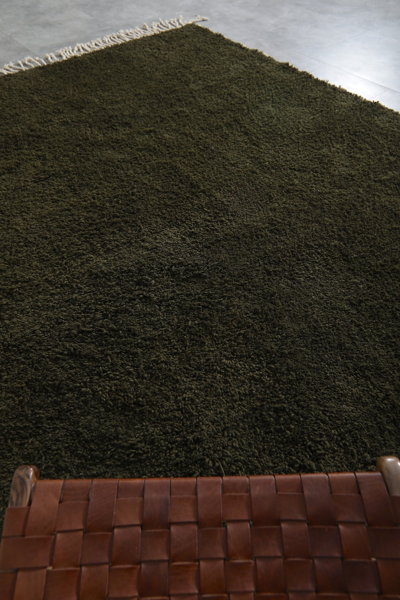 May include: A dark green shag rug with a woven leather seat cushion in front of it.