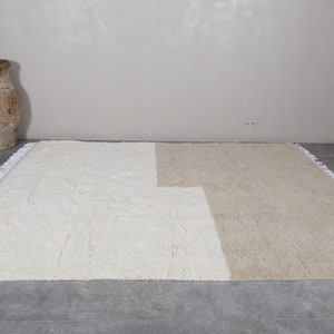 Puede incluir: Una alfombra de &aacute;rea blanca y beige con un borde de flecos. La alfombra est&aacute; hecha de un material suave y esponjoso.