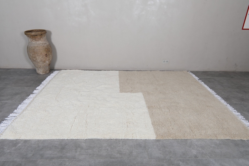 Puede incluir: Una alfombra de &aacute;rea blanca y beige con un borde de flecos. La alfombra est&aacute; hecha de un material suave y esponjoso.
