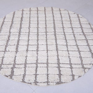 May include: A round, white and gray area rug with a geometric pattern. The rug has a woven texture and a subtle sheen.