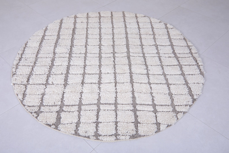 May include: A round, white and gray area rug with a geometric pattern. The rug has a woven texture and a subtle sheen.