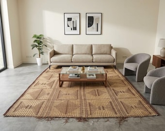 May include: A living room scene featuring a beige sofa, two gray armchairs, and a rectangular coffee table with a glass top. A large, patterned rug in shades of brown and tan covers the floor. Two framed abstract art pieces hang on the wall.