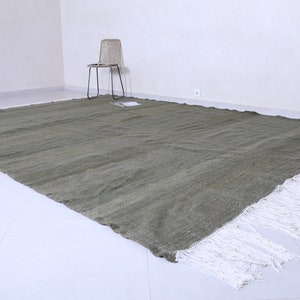May include: A large, rectangular, green rug with white fringe. The rug is made of a woven material and has a subtle texture.