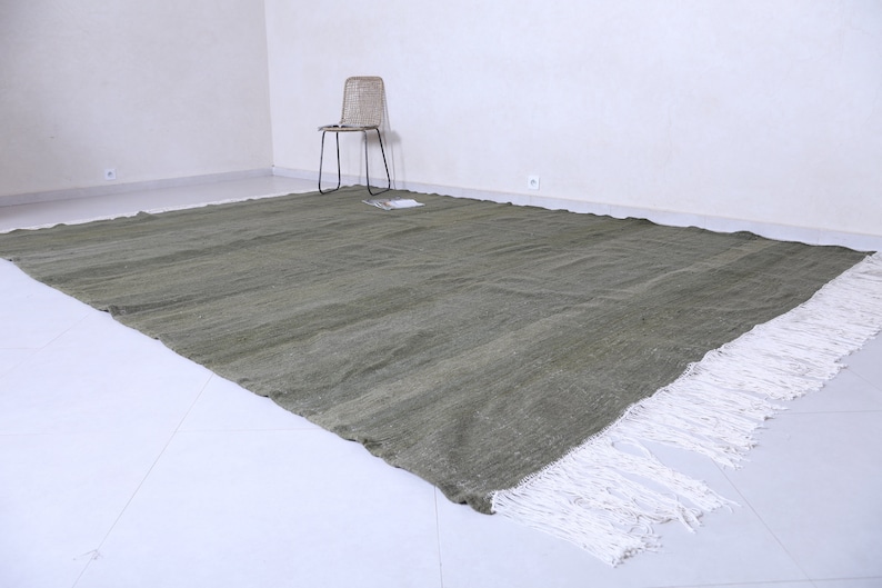 May include: A large, rectangular, green rug with white fringe. The rug is made of a woven material and has a subtle texture.