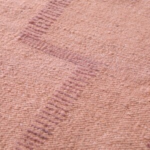 May include: Close-up of a pink woven fabric with a subtle textured pattern. The fabric has a slightly raised, striped design in a darker shade of pink.