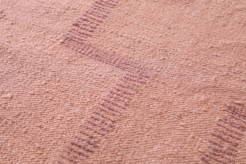 May include: Close-up of a pink woven fabric with a subtle textured pattern. The fabric has a slightly raised, striped design in a darker shade of pink.