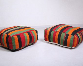 May include: Two colorful striped floor cushions with a white base. The cushions are made of a woven fabric with stripes of red, orange, green, and black.