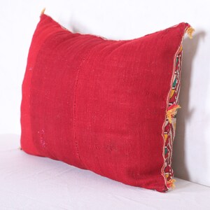 May include: A red pillow with a colorful embroidered border. The pillow is made of a soft, woven fabric and has a rectangular shape.