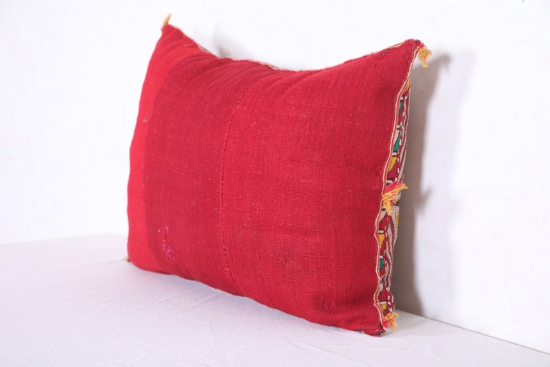 May include: A red pillow with a colorful embroidered border. The pillow is made of a soft, woven fabric and has a rectangular shape.