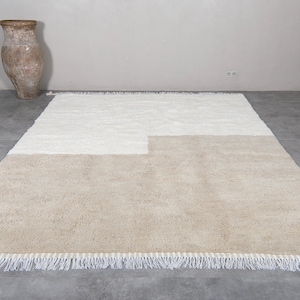 Puede incluir: Una alfombra beige y blanca con un dise&ntilde;o geom&eacute;trico y bordes con flecos.