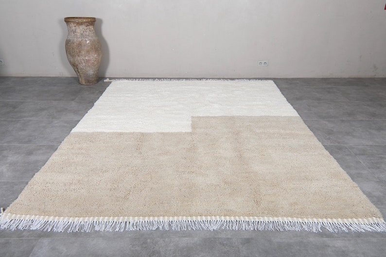Puede incluir: Una alfombra beige y blanca con un dise&ntilde;o geom&eacute;trico y bordes con flecos.