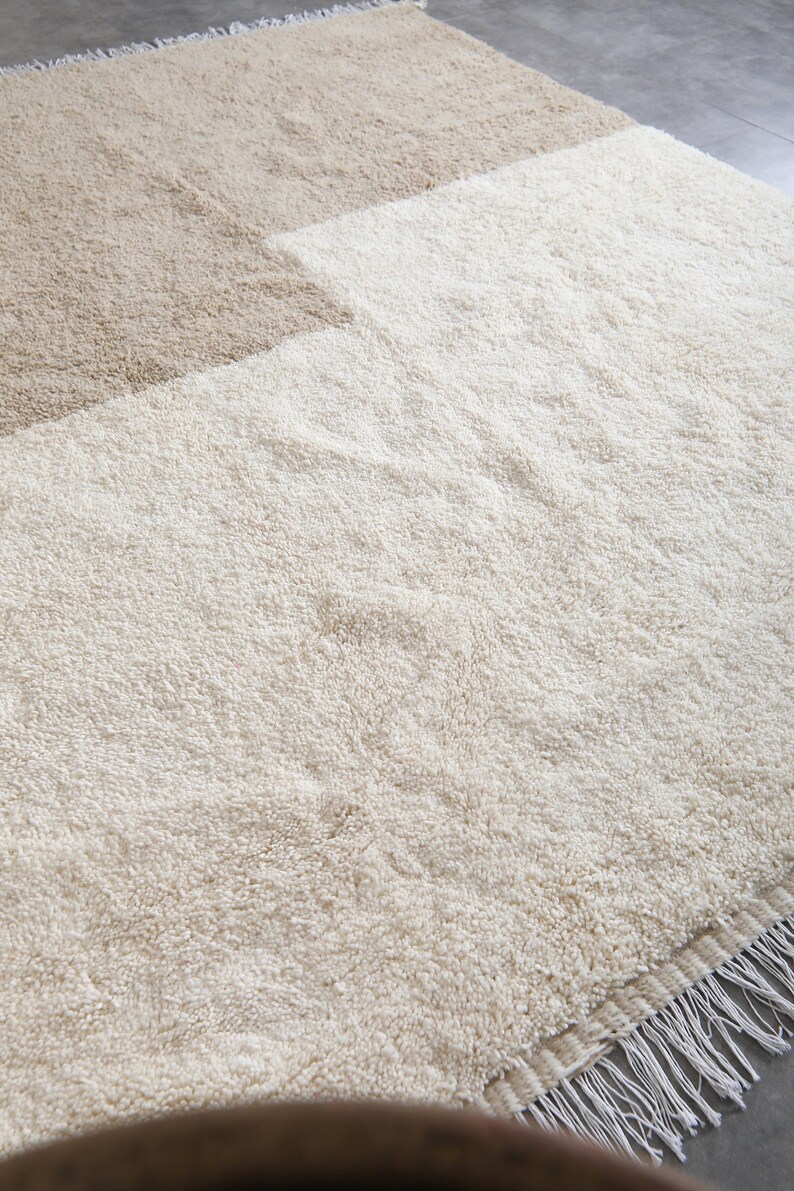 Puede incluir: Una alfombra de pelo beige y blanco con borde de flecos. La alfombra est&aacute; hecha de fibras suaves y esponjosas y tiene un sutil dise&ntilde;o de dos tonos.