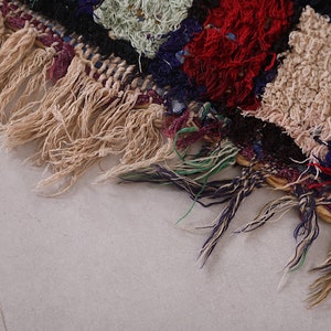 May include: Close-up of a colorful woven rug with fringe. The rug is made of different colored yarns, including red, blue, green, and white. The fringe is a light brown color.