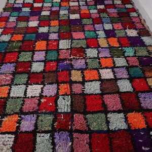 May include: A colorful Moroccan rug with a checkered pattern in shades of red, orange, green, purple, and black. The rug is made of wool and has a hand-woven texture.