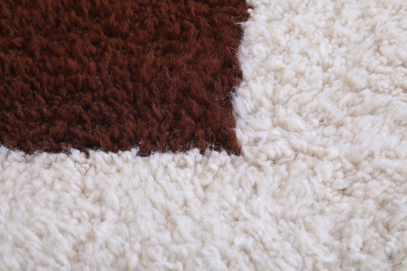 以下が含まれることがあります： 茶色と白のシャギーラグのクローズアップ。ラグは、左上の角に茶色の正方形、右下の角に白い正方形がある幾何学模様です。