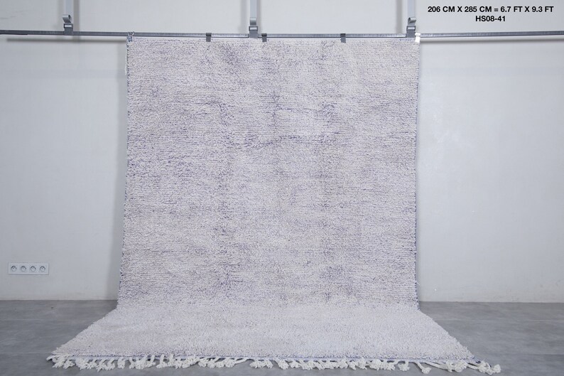 K&ouml;nnte beinhalten: Ein wei&szlig;er und helllilafarbener Shaggy-Teppich mit Fransenbord&uuml;re. Der Teppich h&auml;ngt an einer Wand und misst 2,03 Meter mal 2,83 Meter.