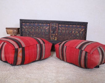 May include: Two red and black striped floor cushions with a wooden chest with colorful geometric designs in the background.