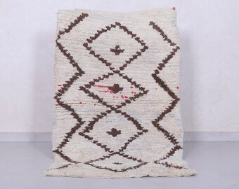 May include: A white Moroccan rug with a brown diamond pattern. The rug has a fluffy texture and is handwoven.