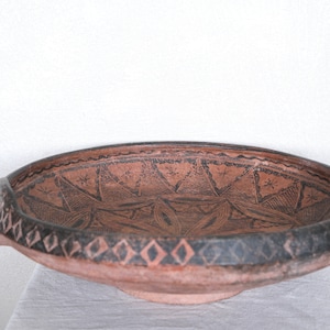Puede incluir: Un cuenco grande, redondo, de terracota con un diseño geométrico negro. El cuenco tiene dos pequeñas asas a los lados.
