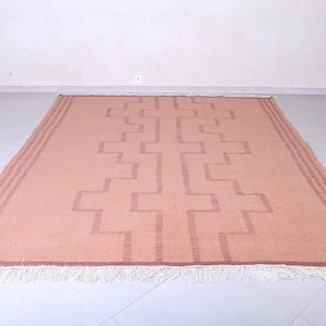May include: A light pink rug with a geometric pattern in a darker shade of pink. The rug has a white fringe border.